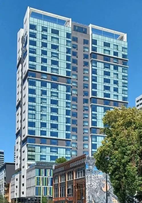 The light blue and white facade of the high-rise of 1700 Webster Street in Oakland, set against a bright blue sky.