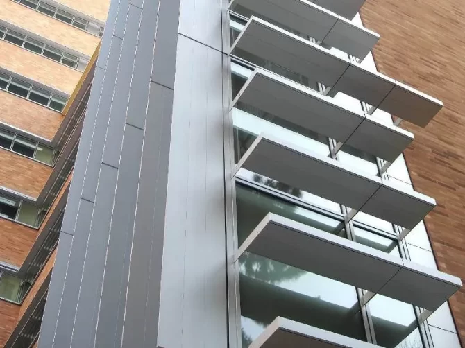 Ground-level upward view of the metal horizontal shading devices and vertical fins on the facade of the Center for Health Sciences South Retrofit, a laboratory / science building at UCLA in Los Angeles, CA.