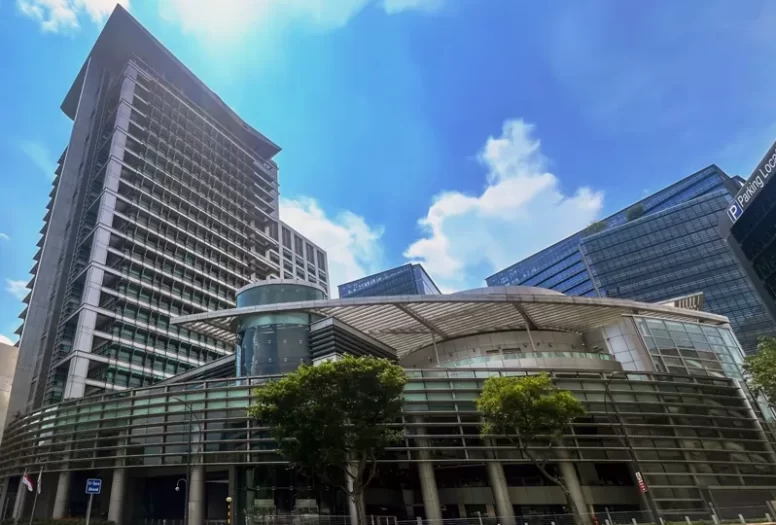 The pale concrete & glass facade of the Singapore Ministry of Education HQ high-rise building set against a bright blue sky.