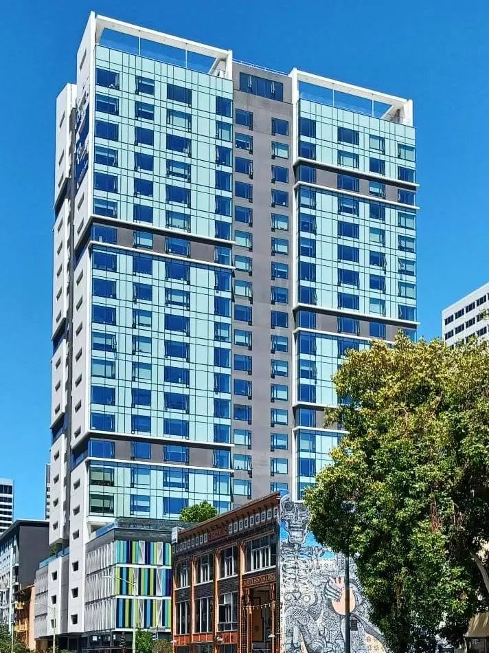 The colorful aquamarine facade of the completed 1700 Webster Street, a high-rise building in Oakland, CA set against a bright blue California sky.