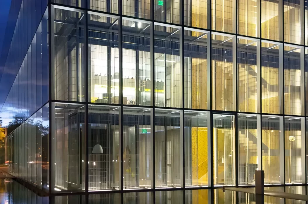Interior lighting shows the steel and glass double-skin facade of the Jaqua Center for Student Athletes at the University of Oregon at night.
