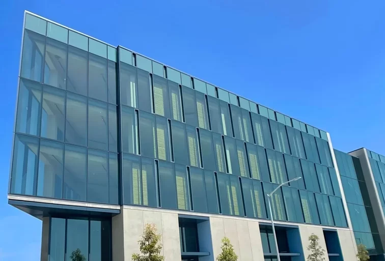 The blue-green glass and steel facade of the 1 De Haro office building in Mission Bay, CA.