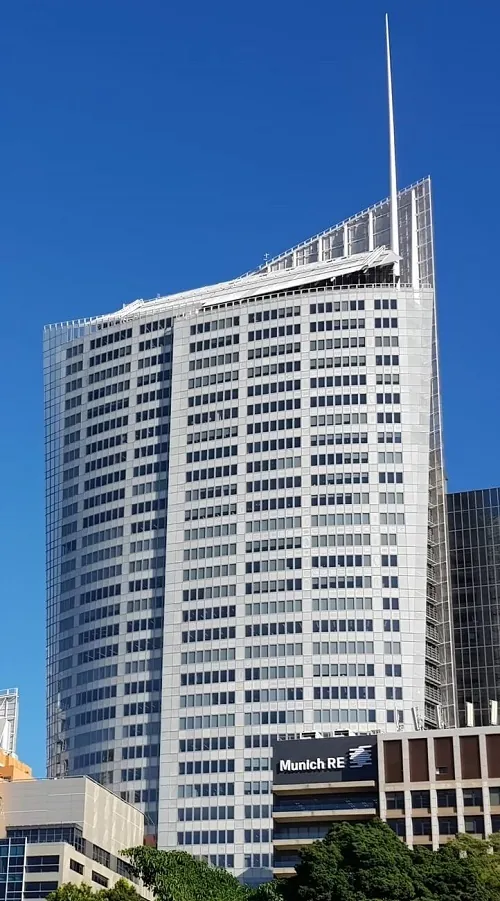 A long distance view of the high-rise white & gray facade of Aurora Place set against a bright blue Sydney, Australia sky.