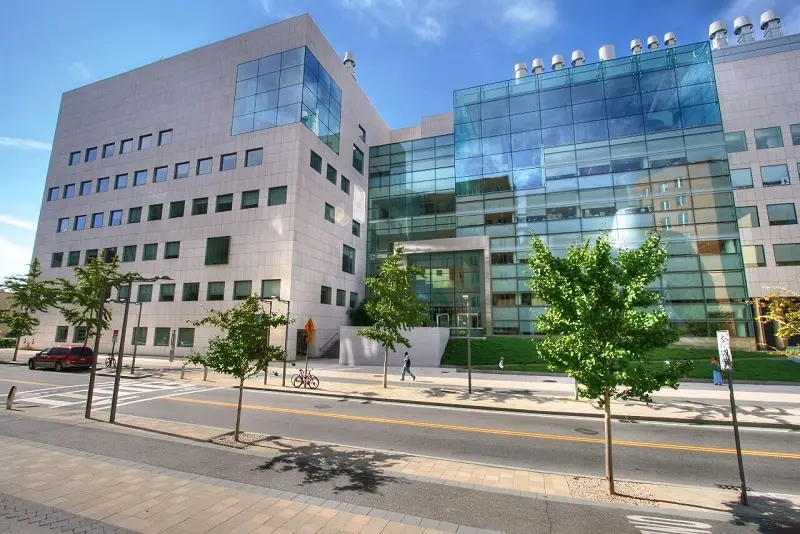 The green glass wall and window-pierced gray concrete facade of the MIT Brain & Cognitive Sciences Complex.