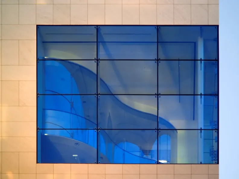 Details of blue glass windows set in a tan stone facade on the MIT Brain & Cognitive Sciences Complex.