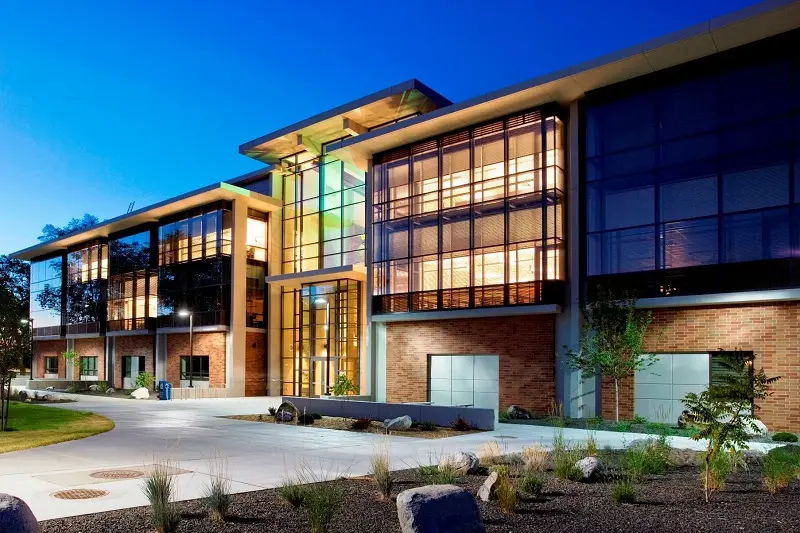 Internal lighting illuminating the front entrance of the sn-w'ey'-mn Building at Spokane Falls Community College under a dark blue night sky.