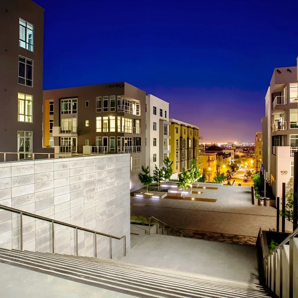 A night-time image of the pastel brown, orange & gray fenestrated facades of the Alta Laguna Multifamily Housing development in San Francisco, punched with square windows and small balconies and set against a dark purple and blue sky.