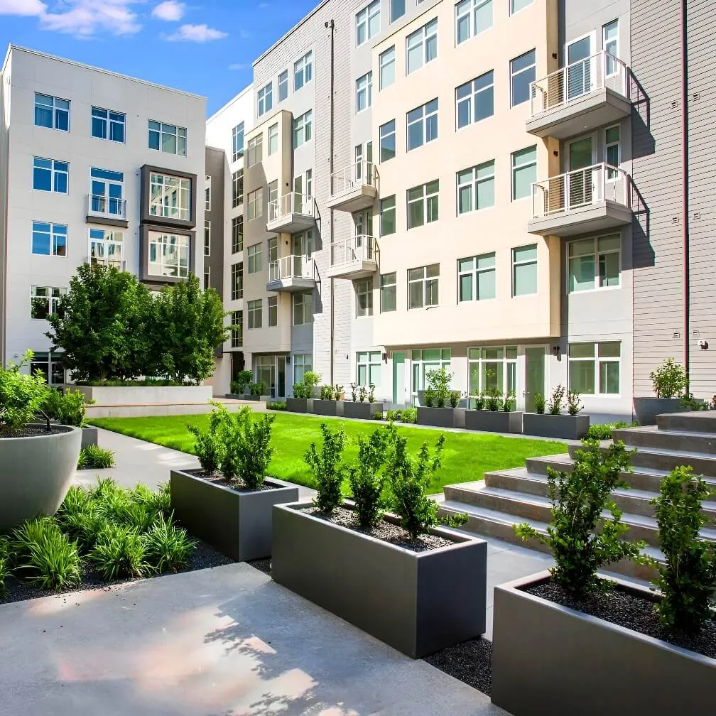 An interior courtyard corner of the Alta Laguna Multifamily Housing development in San Francisco showing a bright green lawn surrounded by pastel colored facades punched with square windows and small balconies.