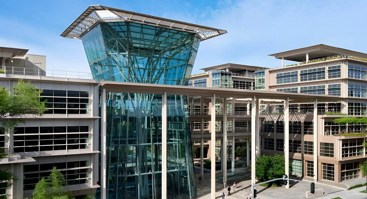 The white concrete, steel and green glass facade of the CalPERS HQ Complex under a bright blue sky.