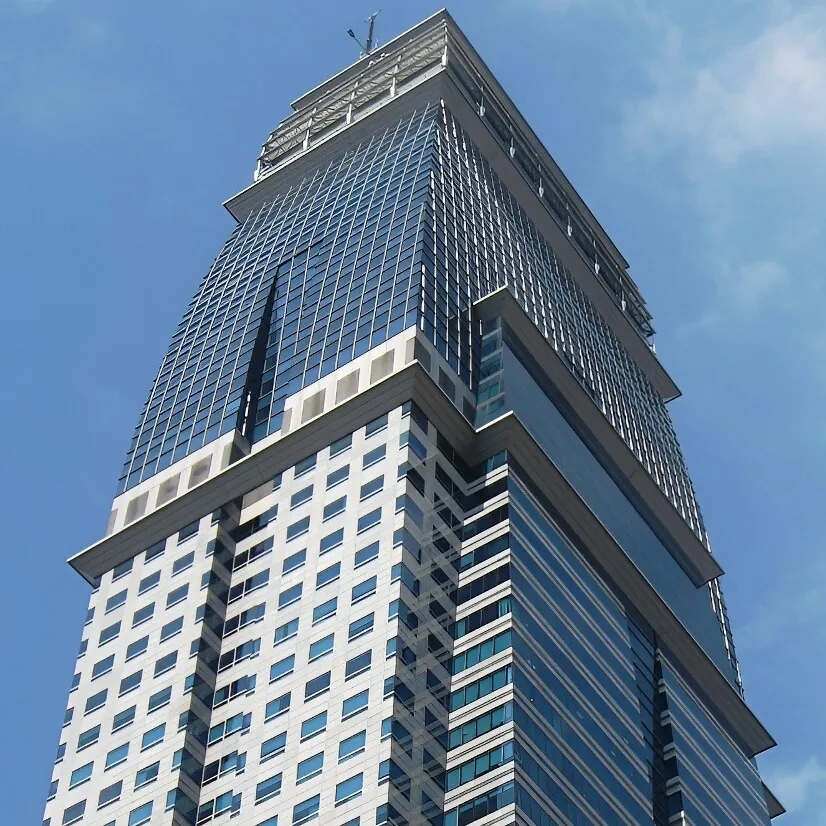 A ground level, upwards view of the top of the white, dark blue and gray steel and stone facade of Capital Tower, a high-rise building in Singapore.