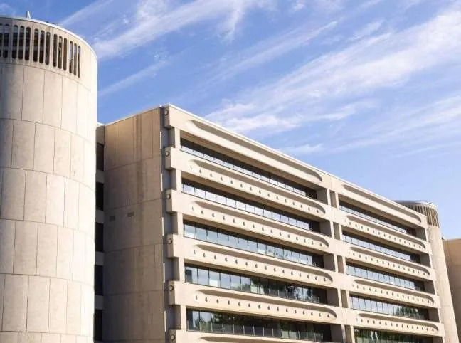 The concrete & glass facade of the Federal Police HQ in Canberra, set against a cloudy blue Australian sky.