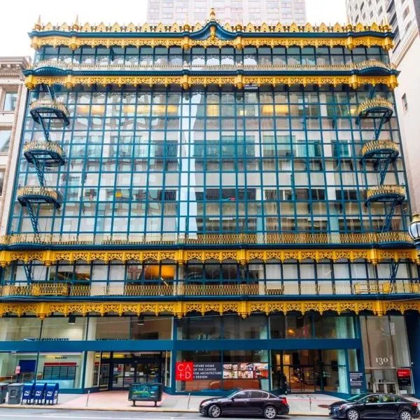 Ornate gold metal friezes, cornices, balconies, and fire escapes set against the blue and gray grid of glass on the facade of the Hallidie Building in San Francisco.